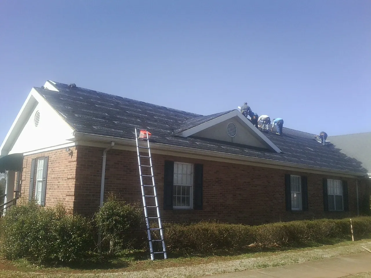 Crew tearing shingles off a brick ranch roof with a ladder set — Emergency Roof Repair work by our crew in West Stockbridge