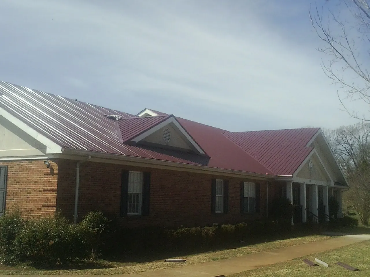 Red metal roof with gabled entries on a long brick building, from a Hail Damage Roof Repair job in West Stockbridge