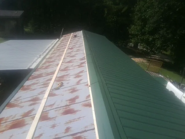 Old rusted panels beside newly installed green metal roofing in West Stockbridge