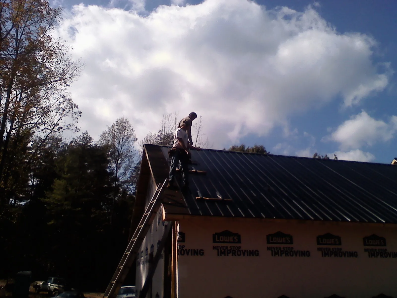 Roofer fastening dark metal panels high against a cloudy sky, from a Roof Inspection job in West Stockbridge