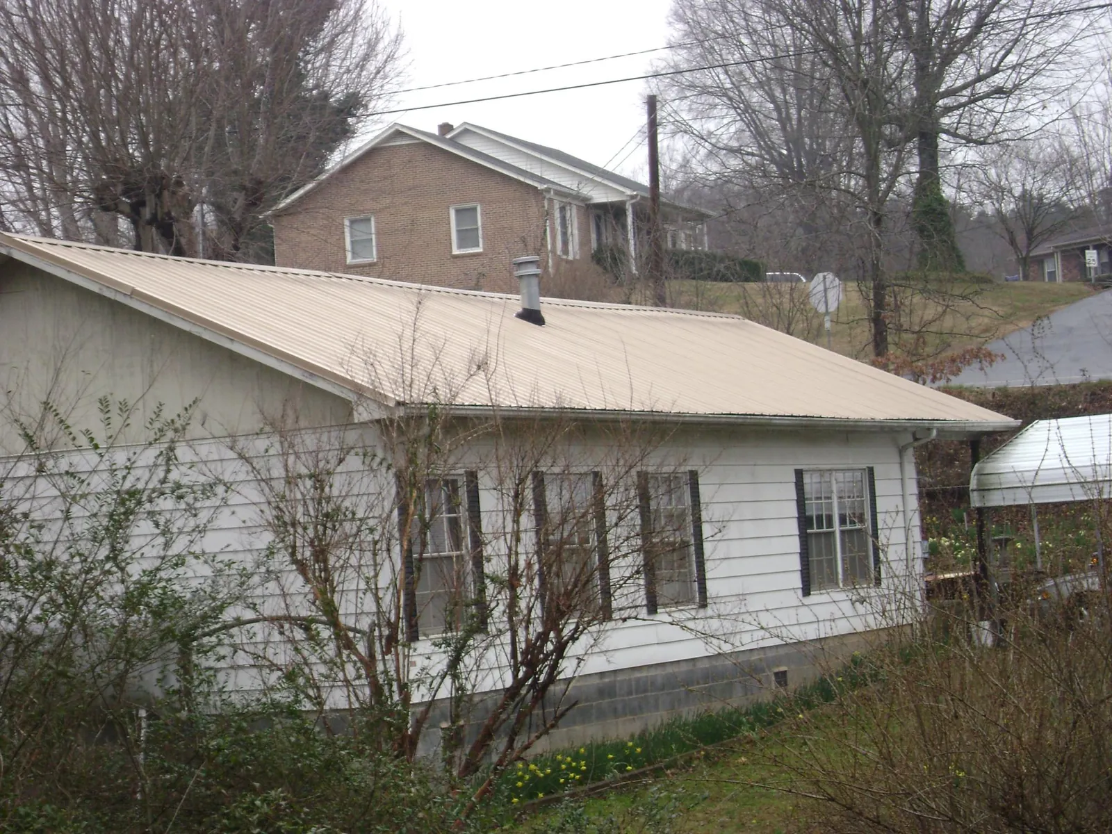 Tan metal roof on a white sided house set into a hillside — Commercial Roofing by Roofing Brothers in West Stockbridge